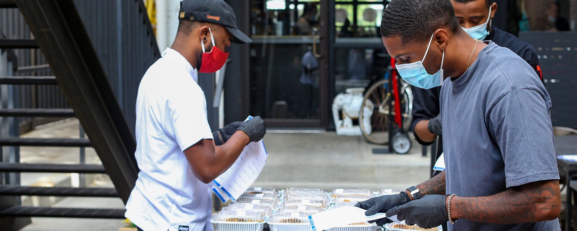 A couple volunteers stand over a table with gloves and masks on preparing food, showing how Capital One is helping their communities